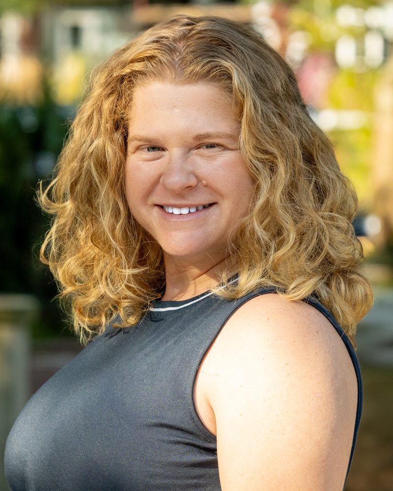 Aly Silver smiling outdoors, with curly blond hair and a dark sleeveless top